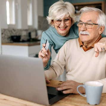 Old couple shopping online at home using laptop