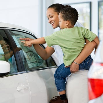 Woman holding toddler and pointing at price sticker on car