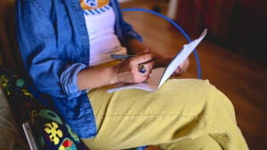 Person with yellow pants reading a document while notating with pen.