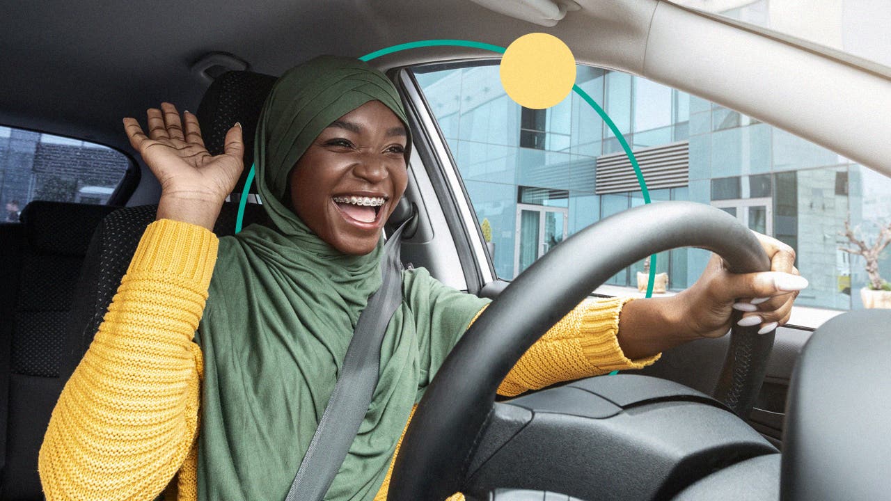 A Black woman wearing a green hijab and yellow sweater smiles happily while inside of a car.
