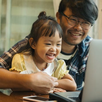 Smiling father holds smiling daughter on his lap while looking at a computer