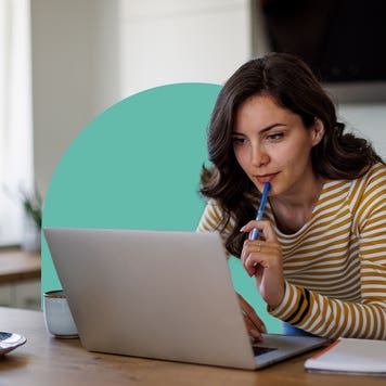 Woman sitting at table looking at open laptop with a blue half circle behind her