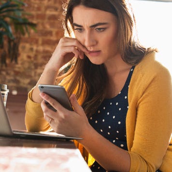 White woman looking at phone with open laptop beside her