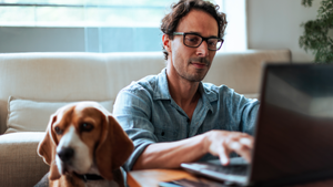 Middle-aged man comfortably working at home on his laptop, sitting on the floor with his Beagle dog by his side.